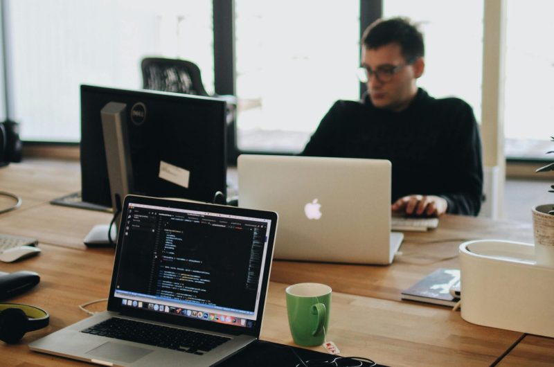 A web developer working on code in a modern office setting with multiple devices.