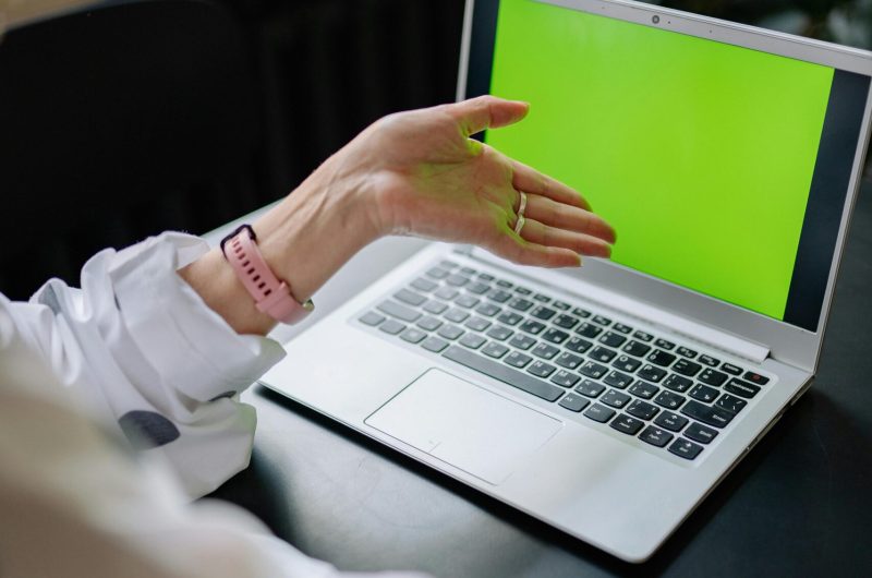 A person points at a green screen laptop indoors, ideal for creative projects.